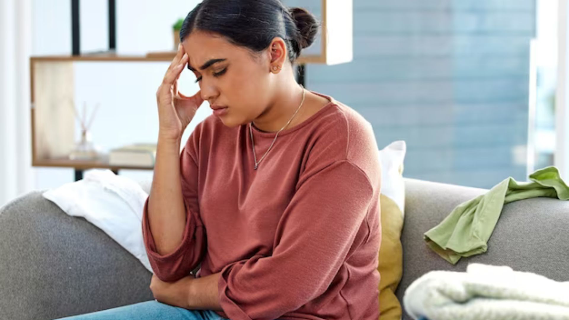 a young lady sitting while touching her head looking sad showing the effect of social media blues on Youths' Mental Health